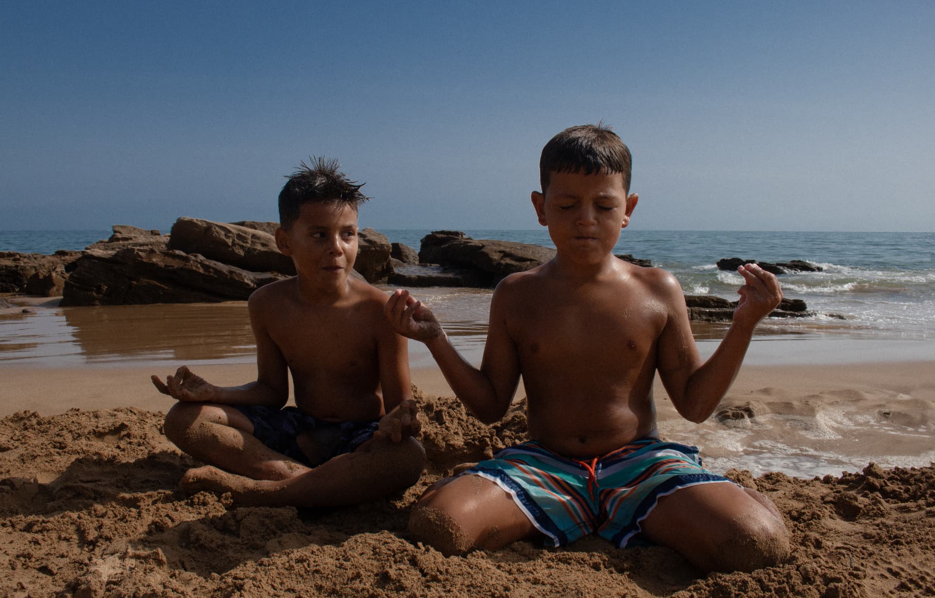 Still — two boys meditating on the sand